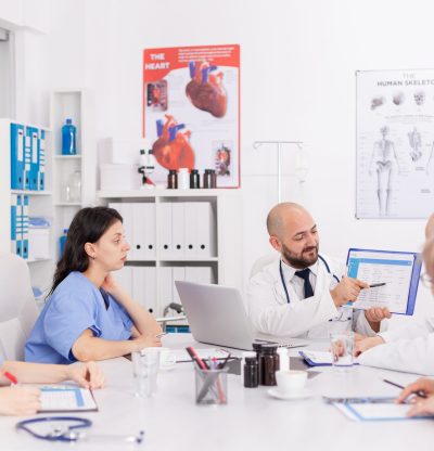 Physiotherapist man doctor holding clipboard in hands presenting healthcare expertise explaining sickness treatment discussing disease diagnostic. Practitioners teamwork working in meeting room